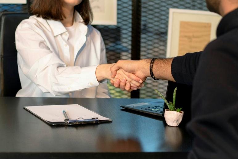 Two people shaking hands across a desk at a job interview